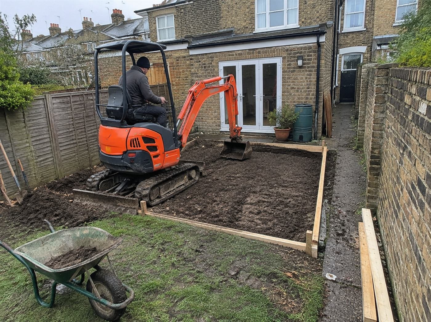 Mini digger working through narrow side access in a London back garden
